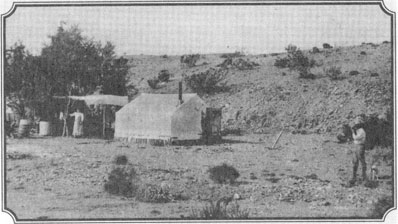 A small, faded black-and-white photograph of the Earp mining camp in the open desert near Vidal, with tents and brush shelters.