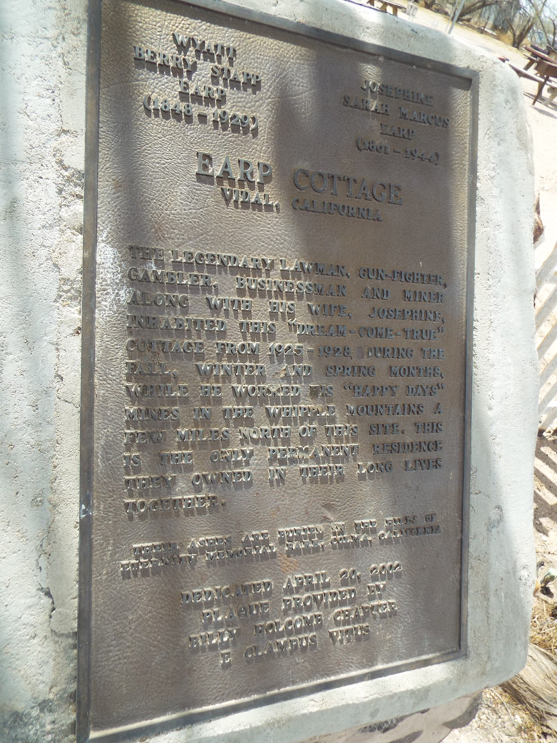 A bronze memorial plaque mounted on a stone-and-cement base in front of the Earp Cottage, commemorating Wyatt and Josephine Earp's residence from 1925 to 1928.