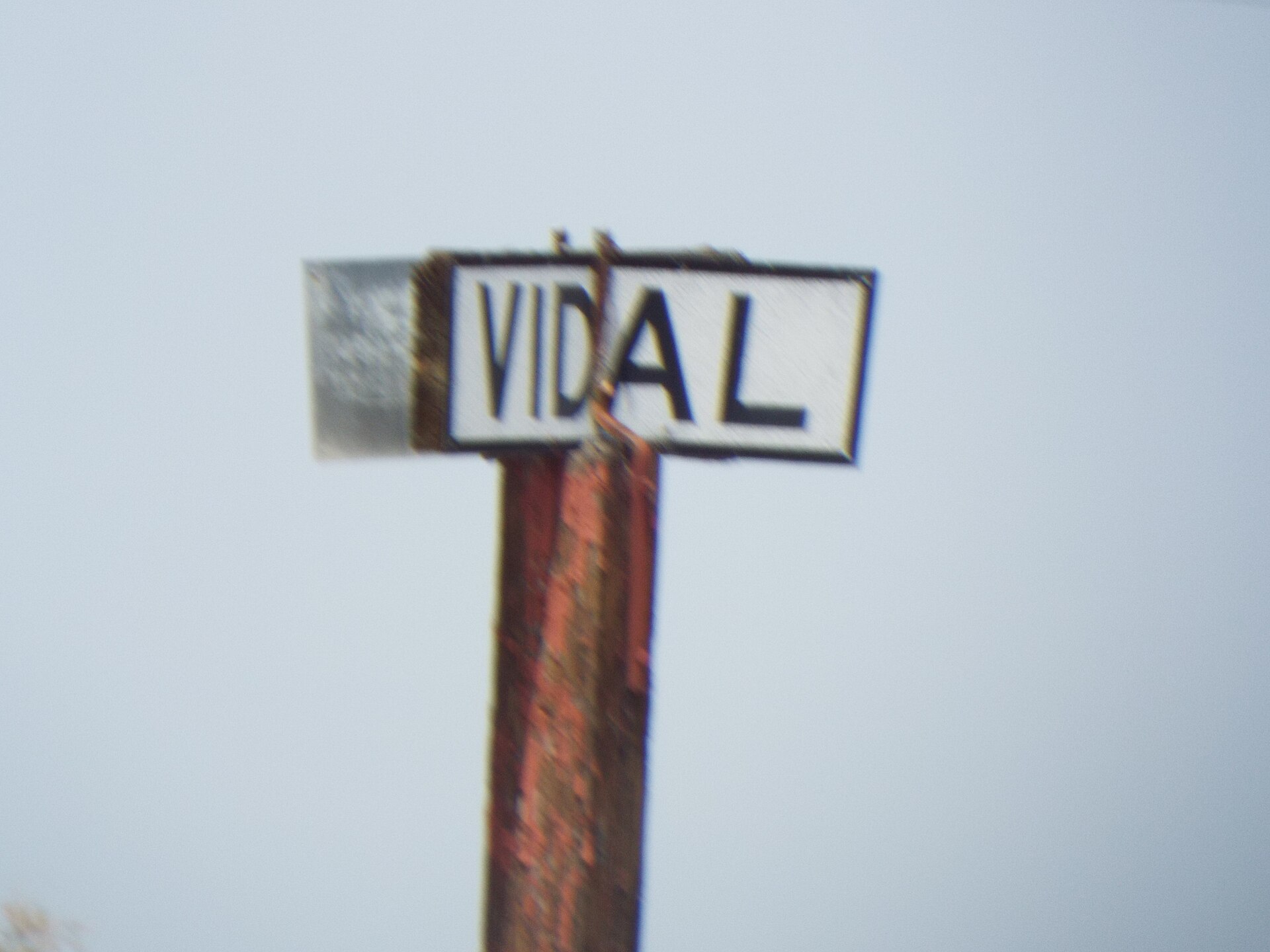 A weathered, bent metal road sign reading 'VIDAL' against a pale desert sky, marking the old crossroad.