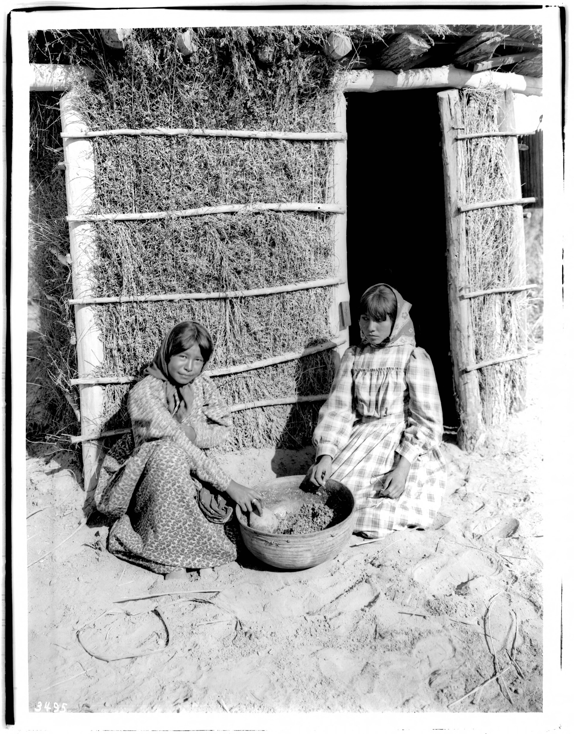 Two young Chemehuevi girls preparing a drink from mesquite beans, photographed around 1900.