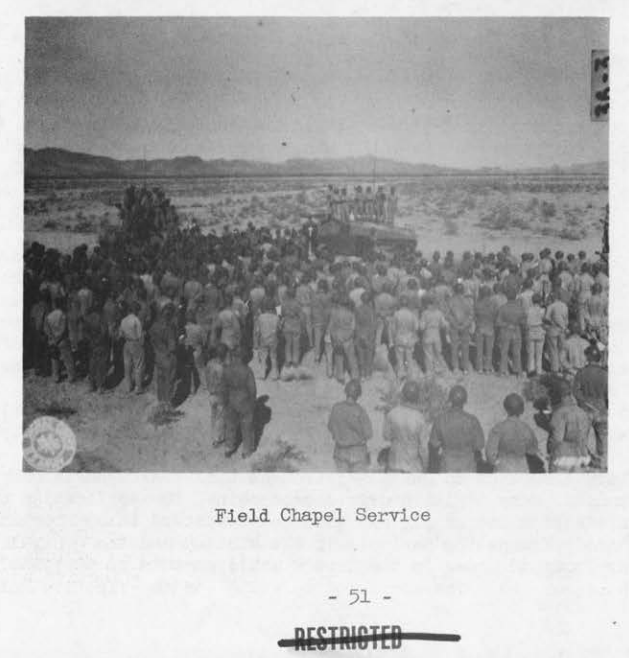 A vast crowd of soldiers standing in the open desert facing a makeshift altar for an outdoor religious service.