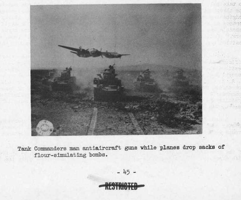 A column of tanks throwing up dust across open desert as a low-flying twin-engine bomber passes overhead during a combined air-ground exercise.