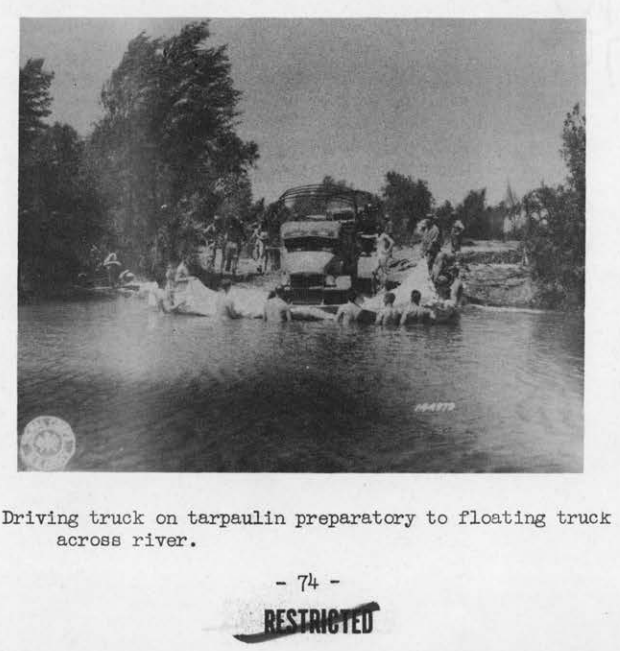 Soldiers wading in a river guiding a truck wrapped in a tarpaulin as it is floated across the water.