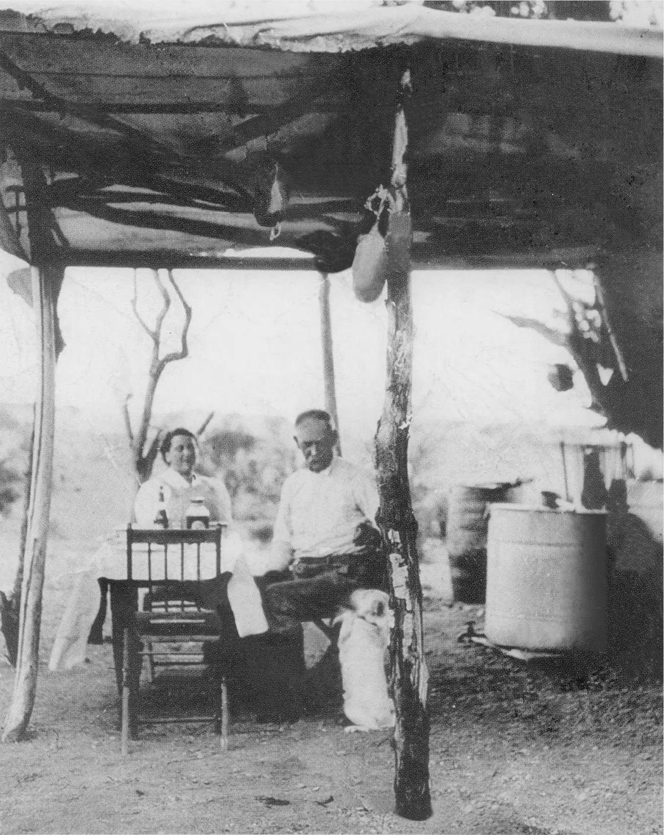 Wyatt Earp and his wife Josephine seated under a desert brush ramada at their Vidal mining camp, circa 1925.